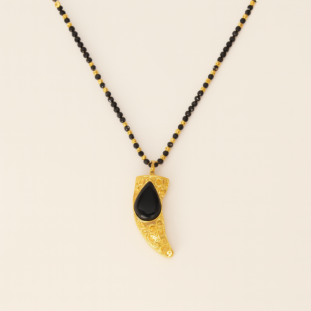 Necklace with black beads and a gold pendant on a beige background