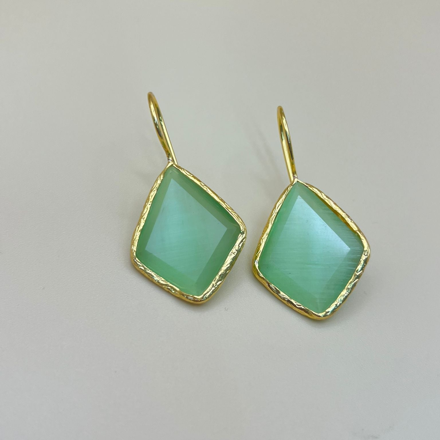 Green gemstone earrings with gold accents on a light gray background