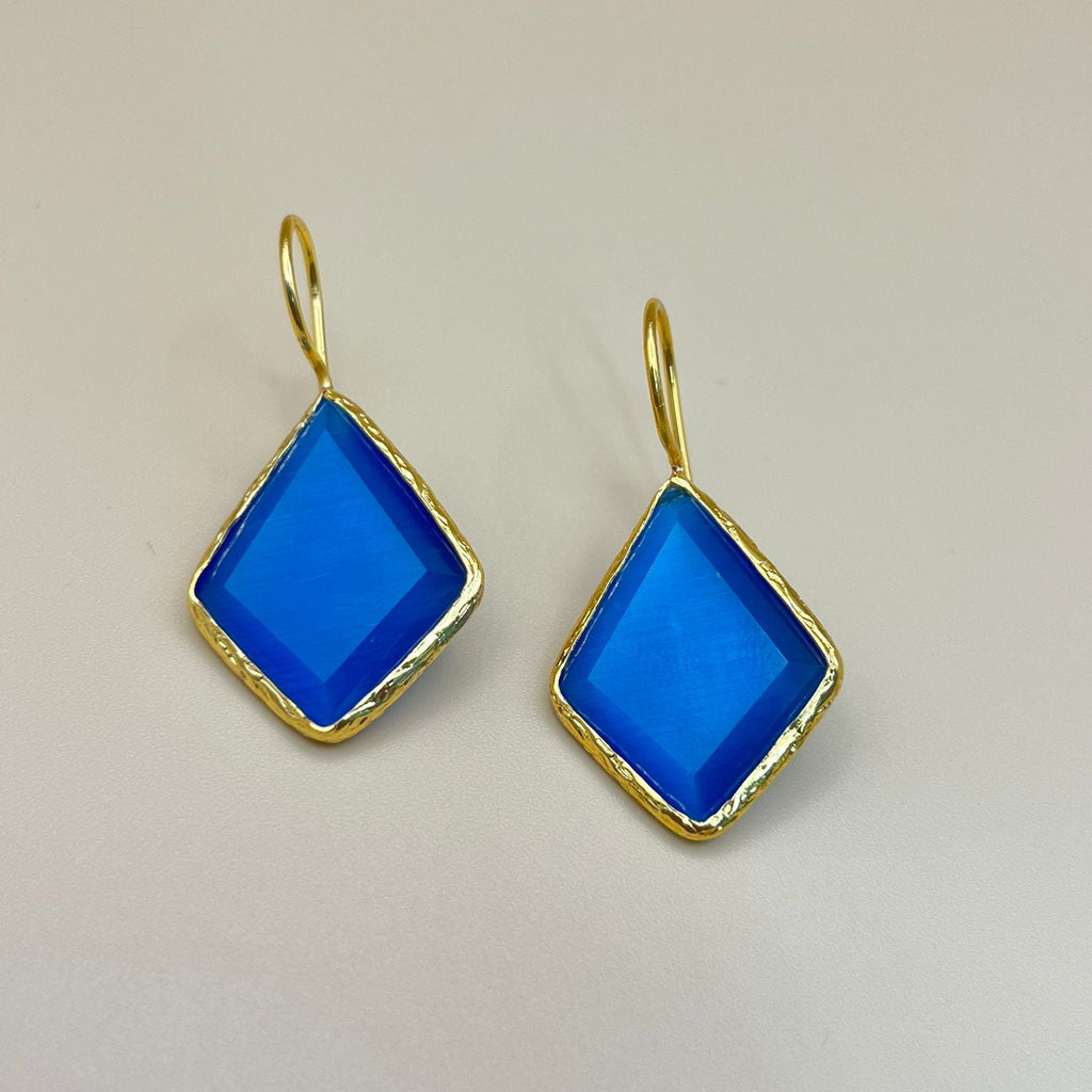 Gold earrings with blue square stones on a beige background