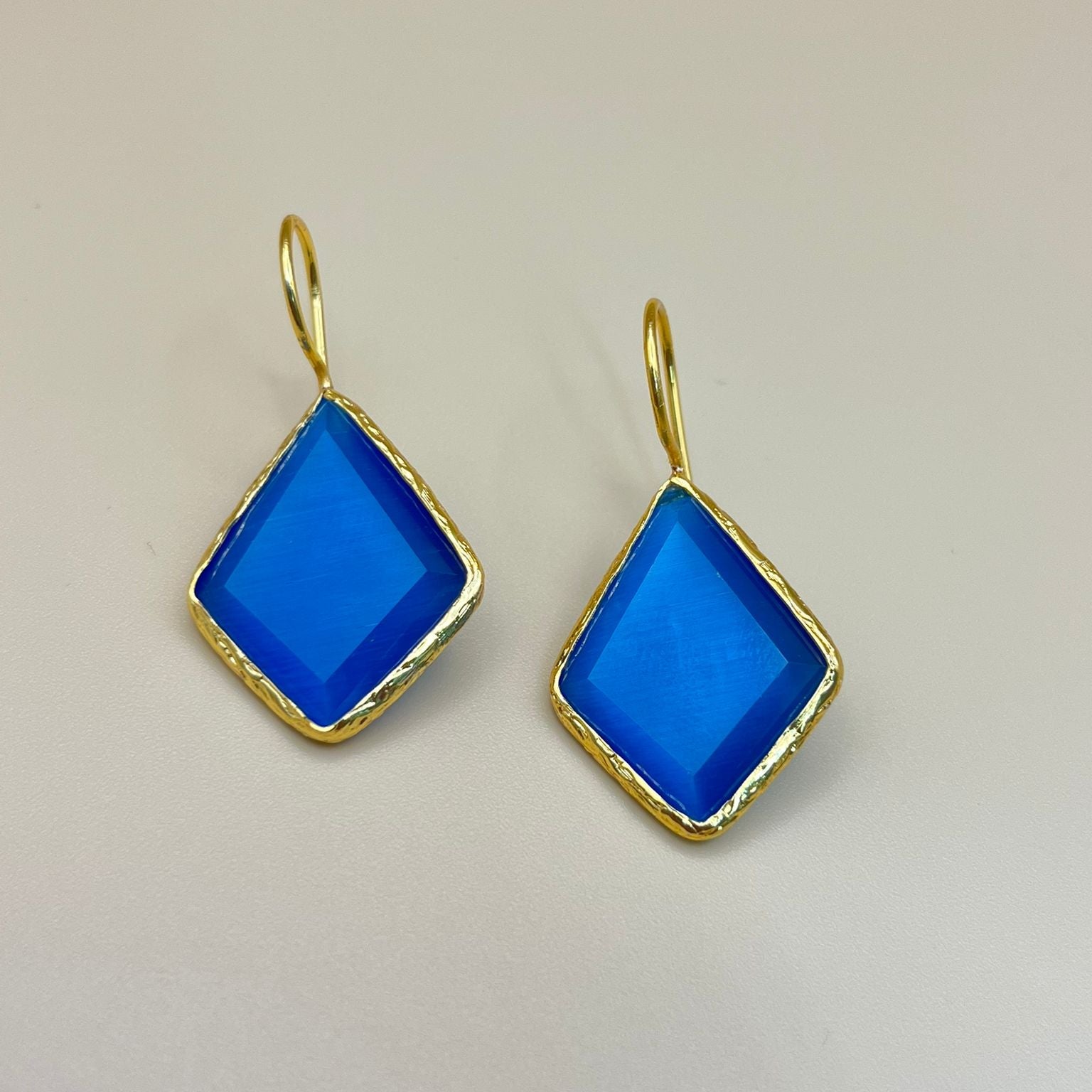 Gold earrings with blue square stones on a beige background