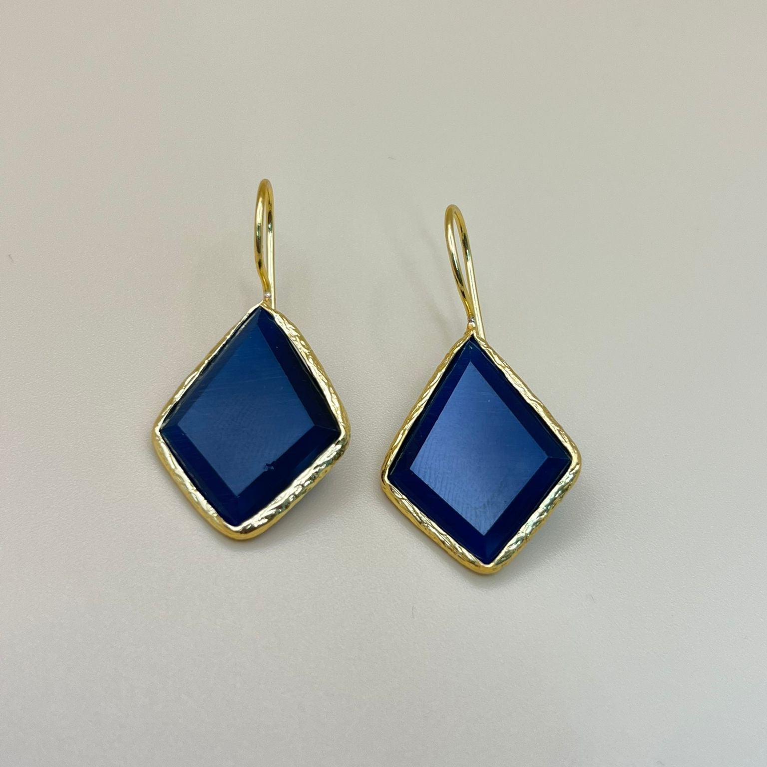 Gold earrings with blue gemstones on a light gray background