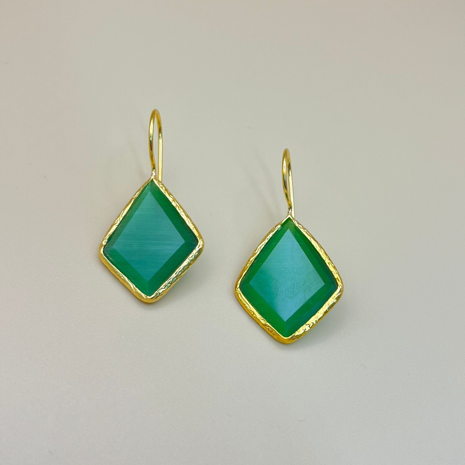 Green earrings with gold frames on a light gray background