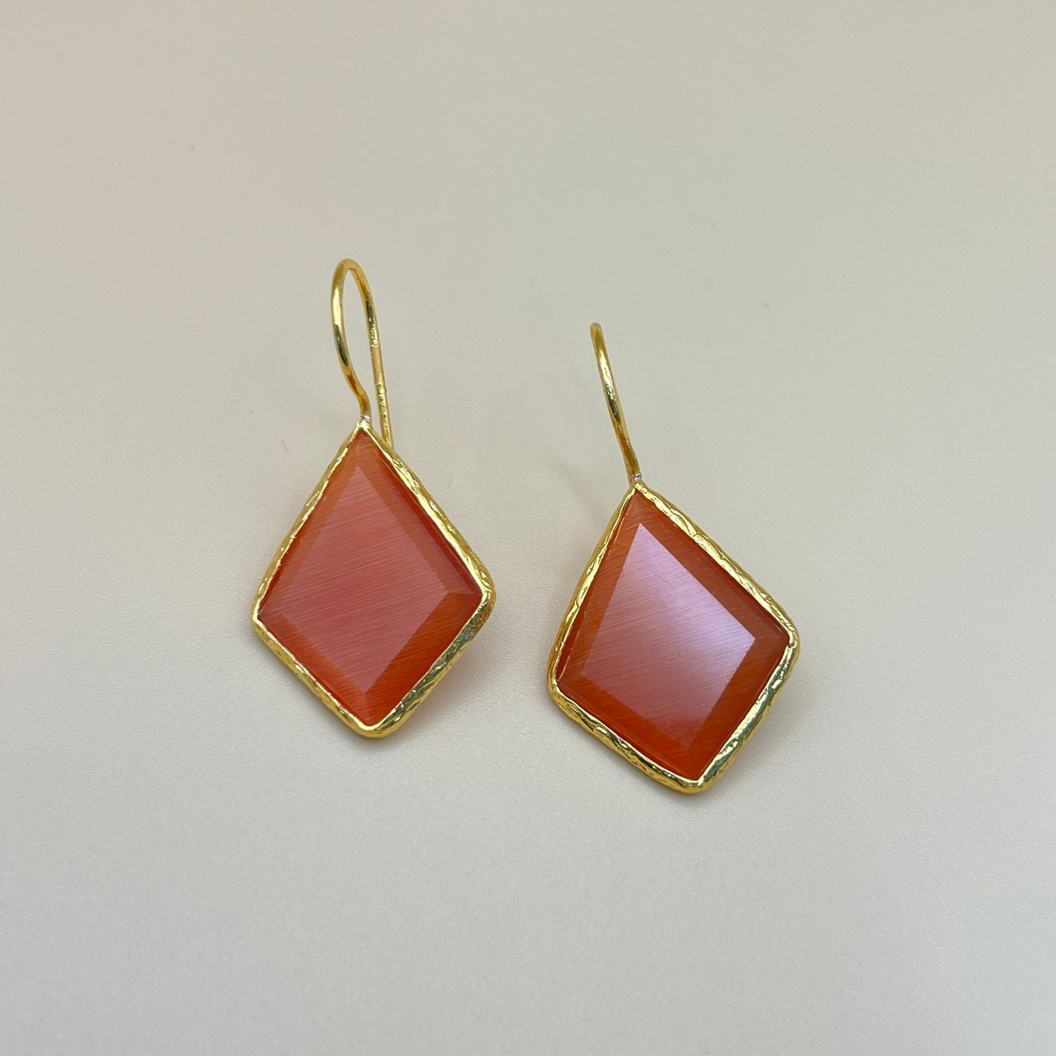 Gold earrings with red gemstones on a light gray background