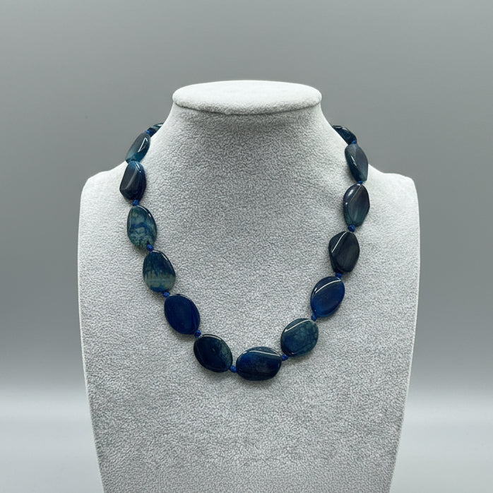 Necklace with blue beads on a gray mannequin bust in a store setting