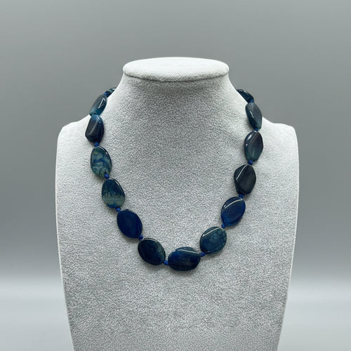 Necklace with blue beads on a gray mannequin bust in a store setting